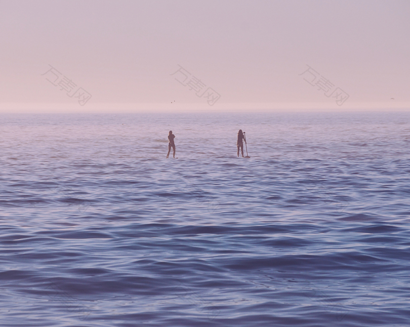 日出时两人站在海面上的冲浪板上
