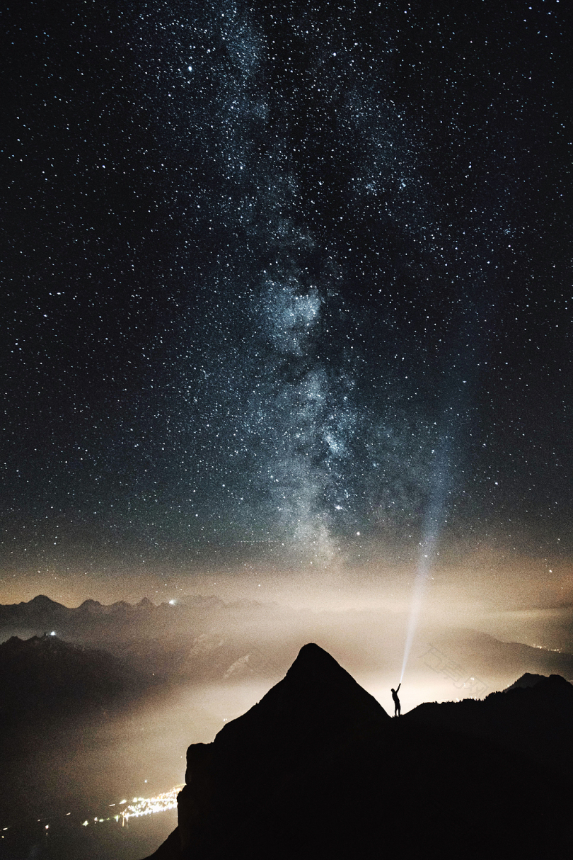 夜晚山顶上人的轮廓指着满天星星的手电筒