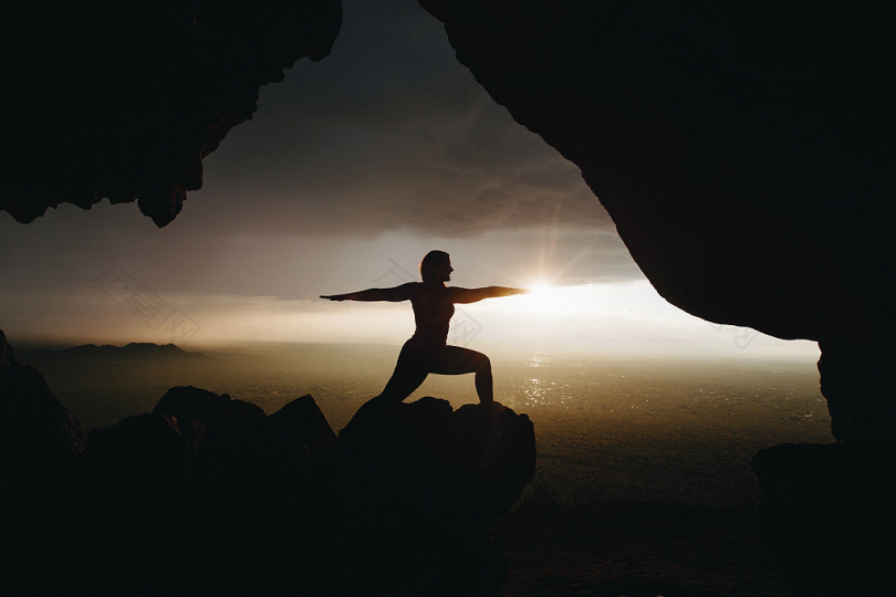 日落时悬崖顶上瑜伽柱人物的剪影