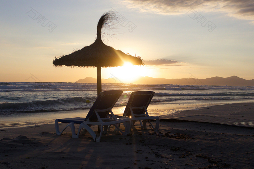 黄金时刻海岸上的两张棕色椅子和伞