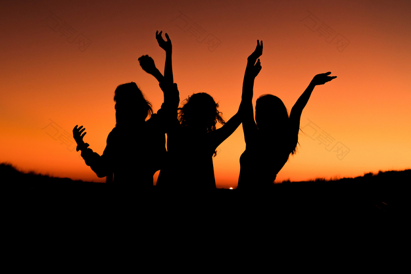 夕阳下舞动的三个女人手在空中的剪影