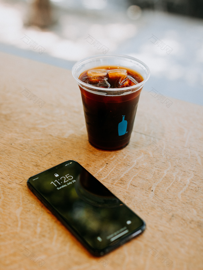 黑色iPhone7旁边的透明一次性杯子里盛满了冰块的饮料