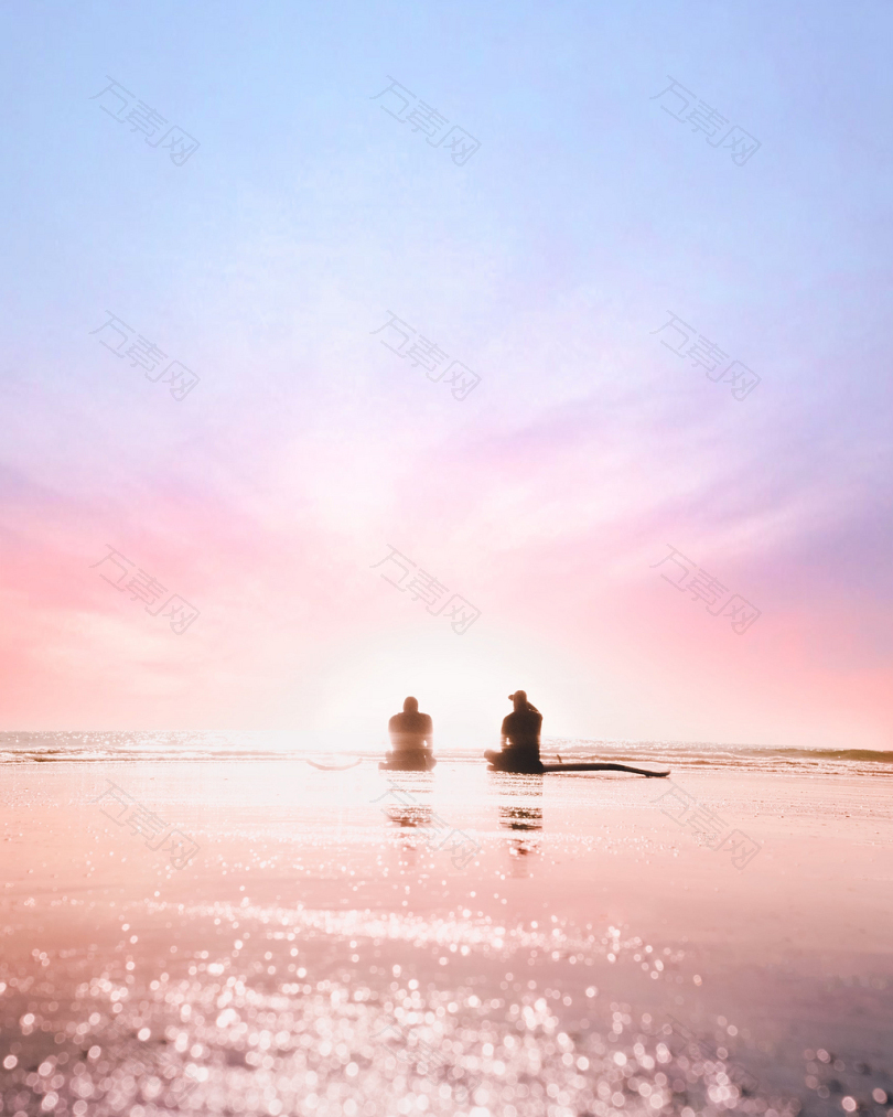 黎明时两个人坐在海边的剪影