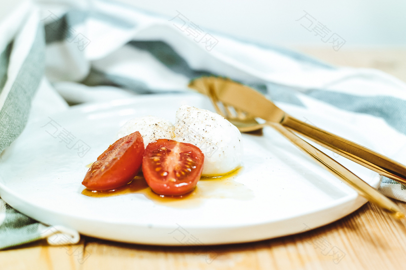 黄铜刀叉旁白盘子上切碎的西红柿和莫扎里拉干酪