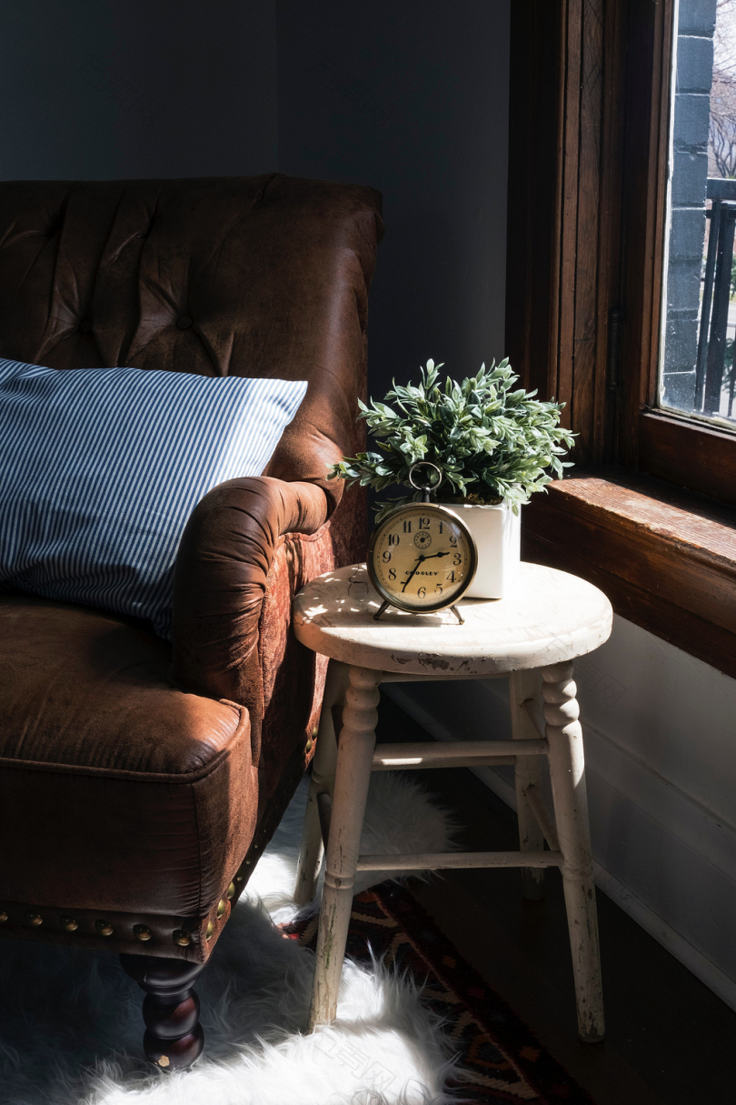 棕色皮革衬垫沙发椅旁白色圆形木凳配圆形灰色金属钟