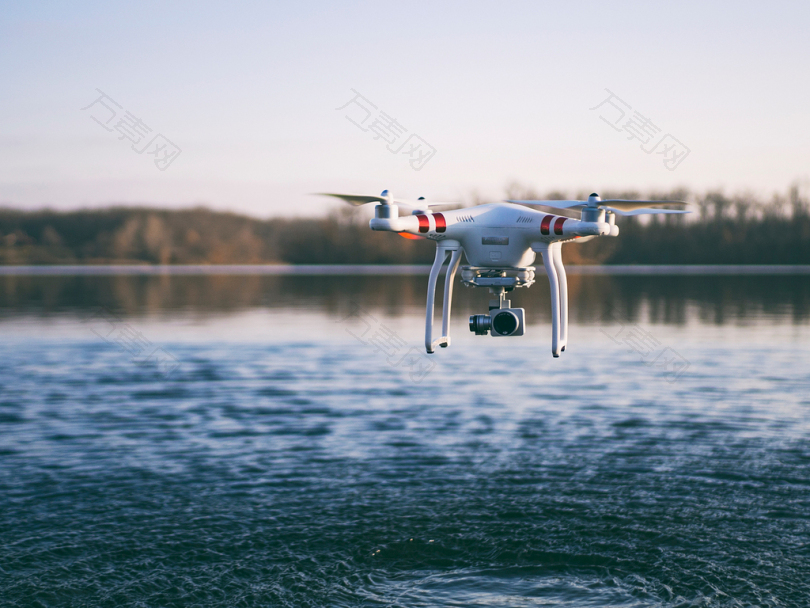 白色四翼无人机在水面上空飞行