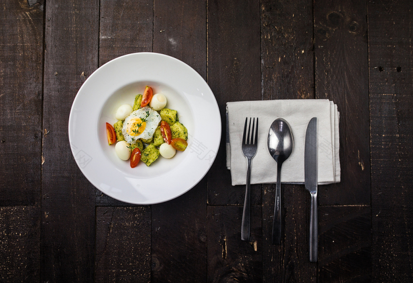 在精美的餐具中在圆形的白色陶瓷盘子里有煎蛋鹌鹑蛋红番茄片和青椒片