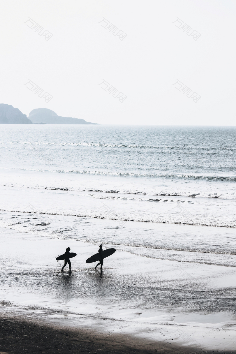 两个人白天在海滩上抬冲浪板
