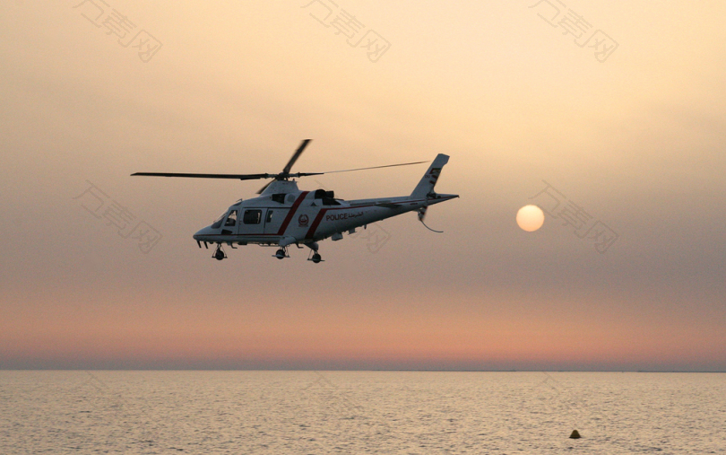 白色和红色直升机在日落时飞越大海