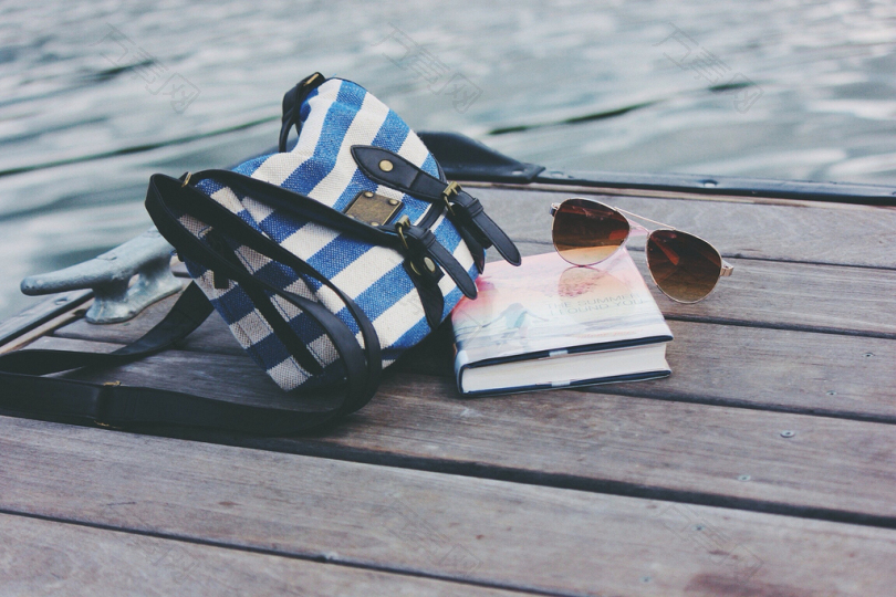 白天在海港附近的书和太阳镜附近的蓝白条纹交叉袋