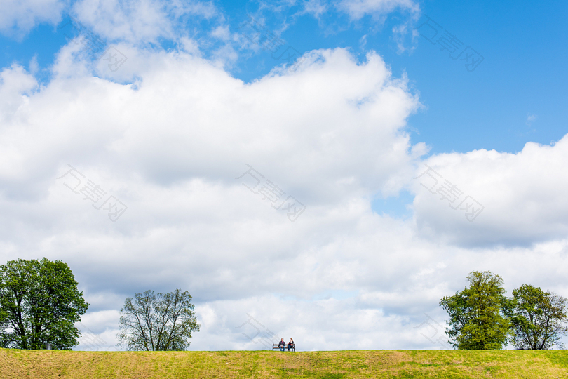 白天坐在白云下四棵高大绿树之间的长凳上的两个人