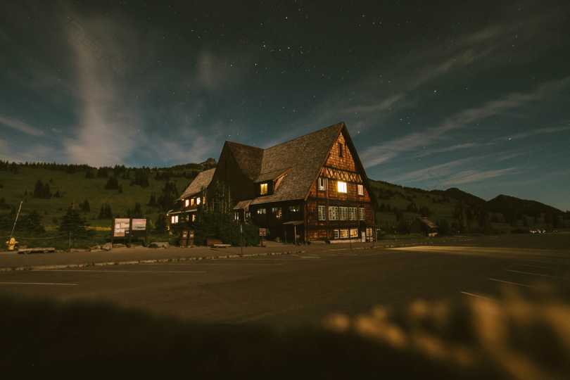 傍晚时分一个大的小木屋从里面照亮了一片有山的田野